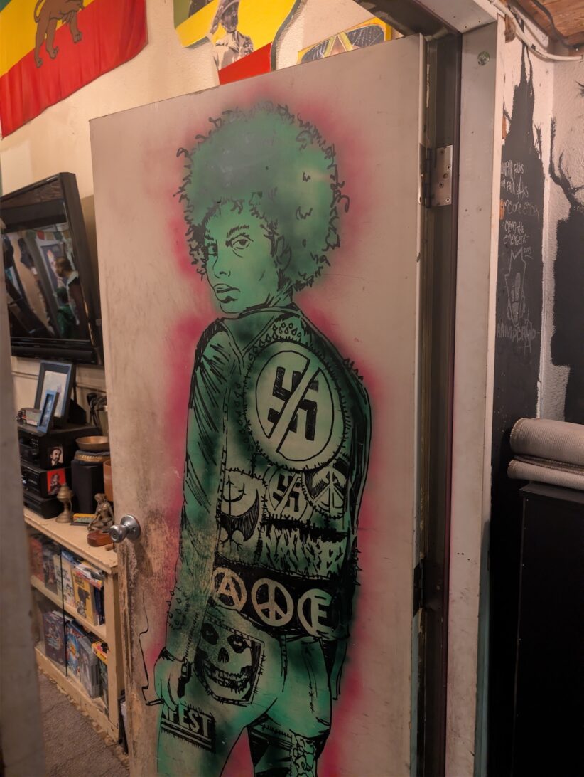 Art on the back of a door depicting a woman in a denim jacket and jeans covered in patches