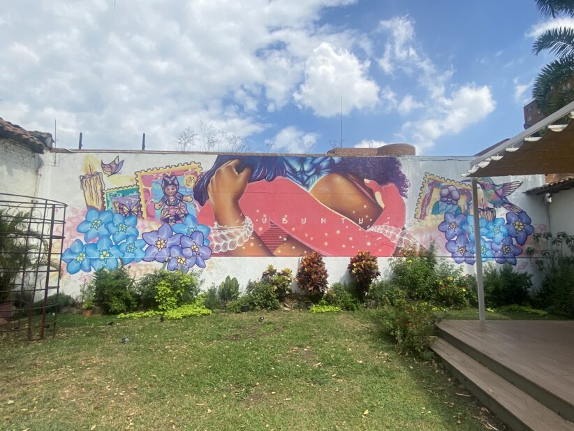 A yard with a mural painted on a wall with the word ubuntu and two individuals embracing