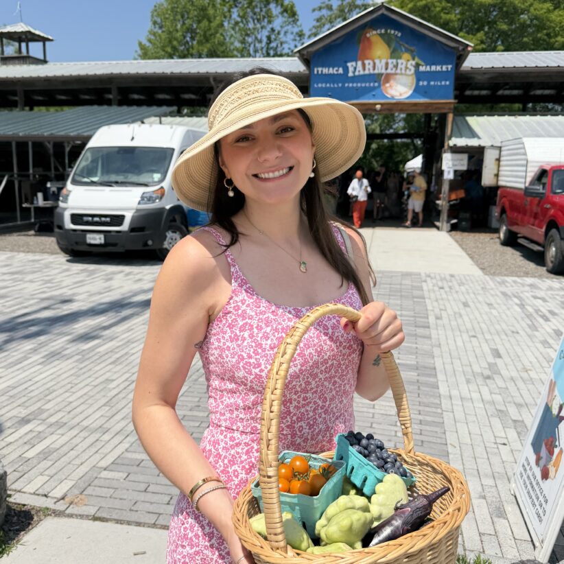 Jordan Deskins stands outside the Ithaca Farmers' Market holding a basket of fresh produce