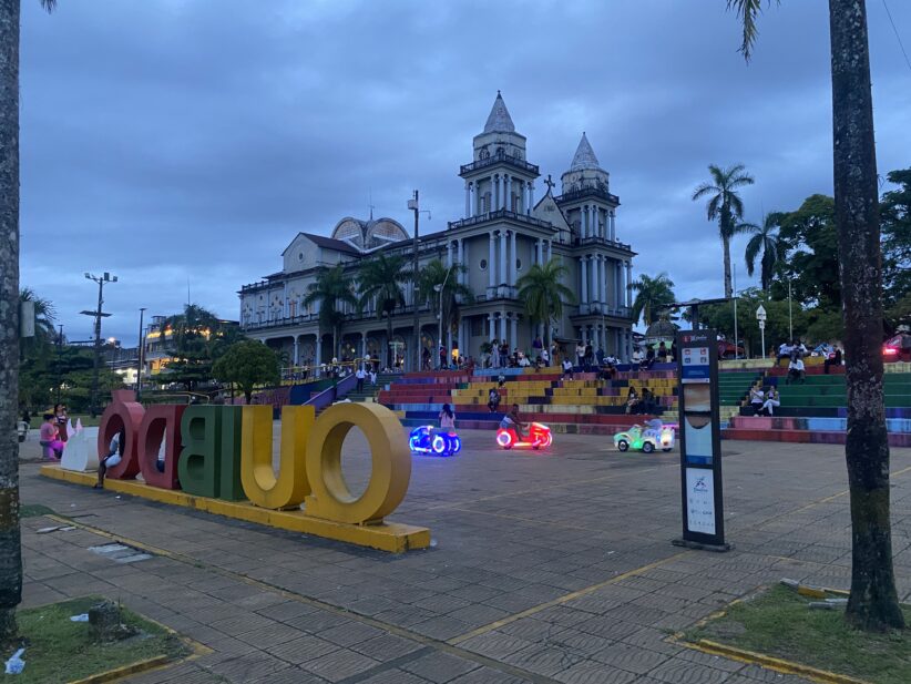 A plaza at dusk with kids riding light up cars in front of backwards letters that spell out the town's name, Quibdo