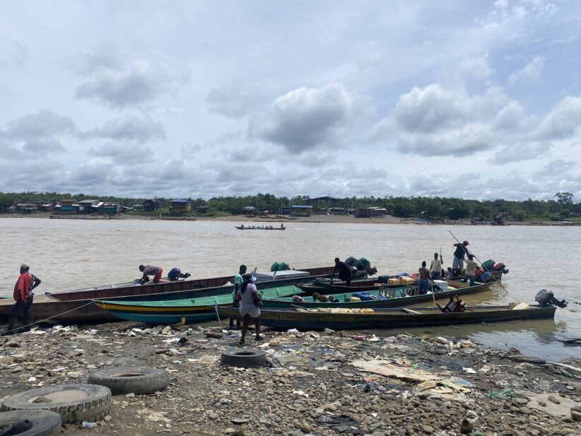 Long canoe-like boats are pulled up on a rocky shore with people in and around them