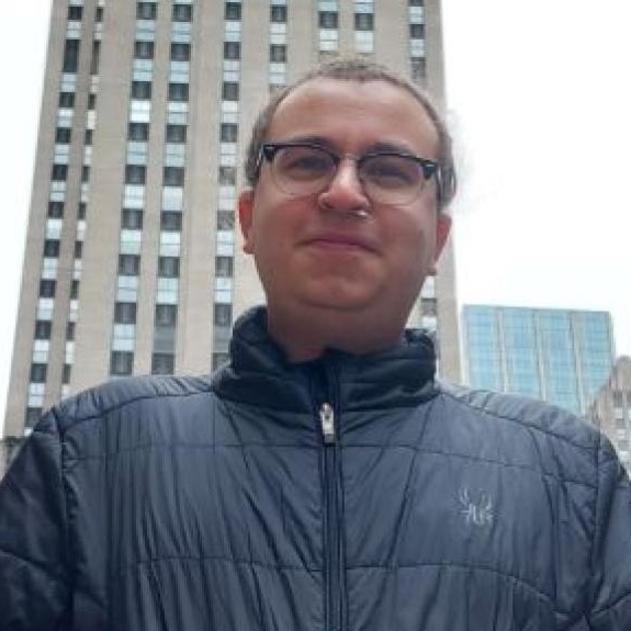 Zander Lynch stands outside with tall buildings looming behind him