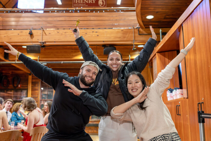 Three students pose for a photo with one of them holding a trivia trophy in hand