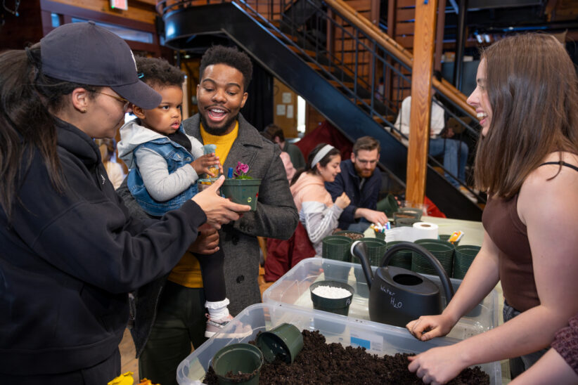 Student parents hold their child and listen to a grad student explain a science station