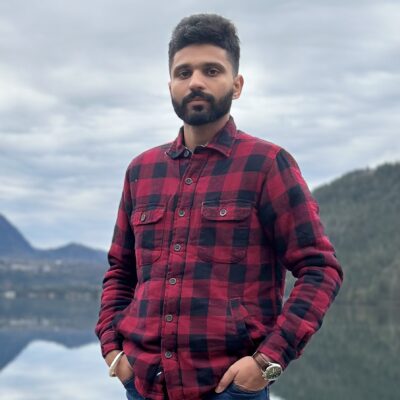 Preetaman Bajwa stands outside with a lake and mountains behind him
