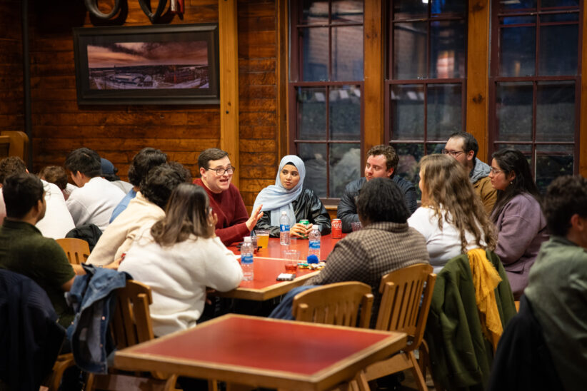 Students sit around a table at the Barn and chat during a TGIF event